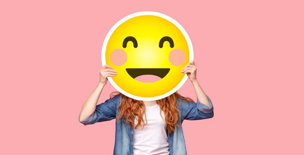 Zrzka dívka skrývá svou tvář za šťastný úsměv emoji — Stock fotografie