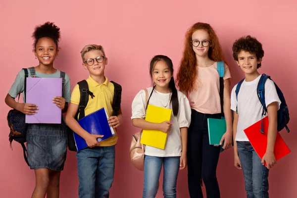 ピンクの背景にバックパックとコピー本を持つ学校のための準備ができている子供たちの多民族グループ — ストック写真
