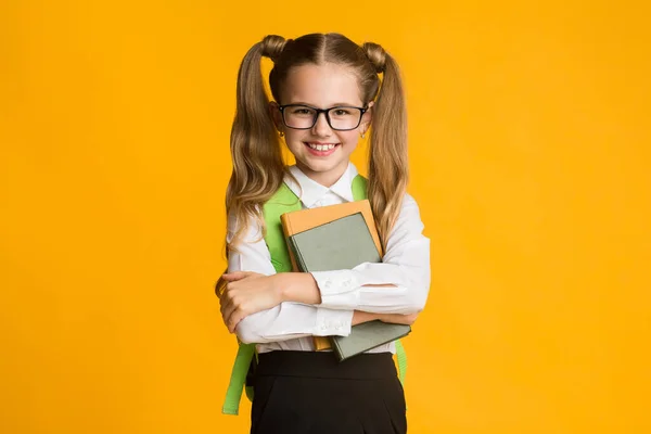 Usmívající se základní studentská dívka objímací knihy na žlutém pozadí studia — Stock fotografie