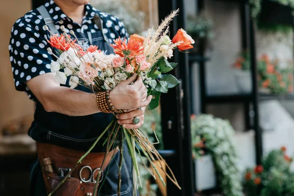 Kompozycja kwiatowa w rękach profesjonalisty. Kobieta w fartuchu, z narzędziami sprawia, bukiet w kwiaciarni — Zdjęcie stockowe
