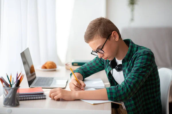 Seriöser Schüler macht Hausaufgaben in seinem Zimmer, schreibt in Notizbuch — Stockfoto