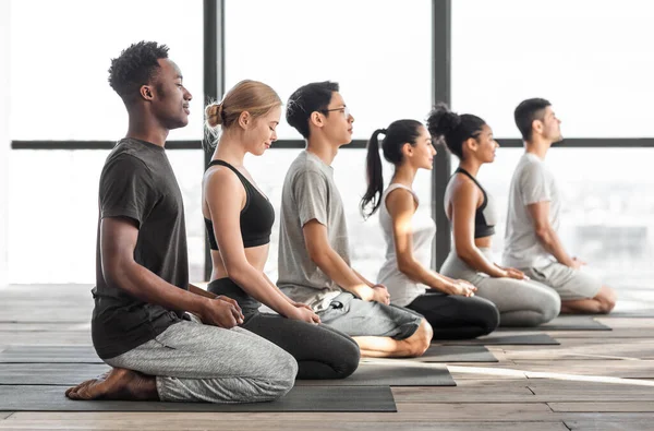Hombres y mujeres multirraciales felices practicando yoga y meditando juntos en el estudio — Foto de Stock
