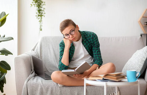 Annoiato adolescente seduto sul divano con libro — Foto Stock