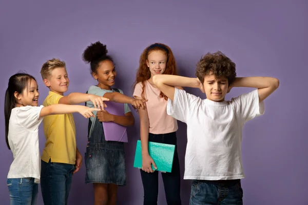 Bullismo a scuola. Crudeli scolari molestare infelice ragazzino su sfondo lilla — Foto Stock