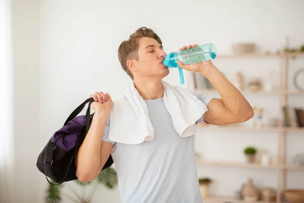 Health care and workout. Slender guy drinks water from bottle and holds sports bag — Stock Photo, Image