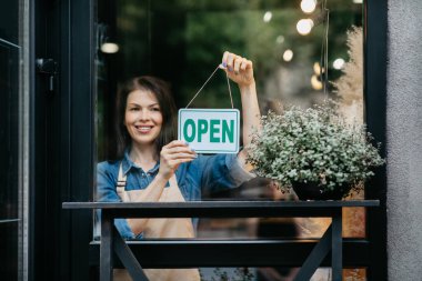 Mutlu kız çiçekçi dükkanı açıyor ve isim levhasını açık yazıyor.