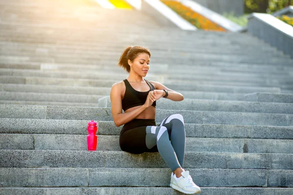 Africano menina fitness sentado em escadas, verificando em smartwatch — Fotografia de Stock