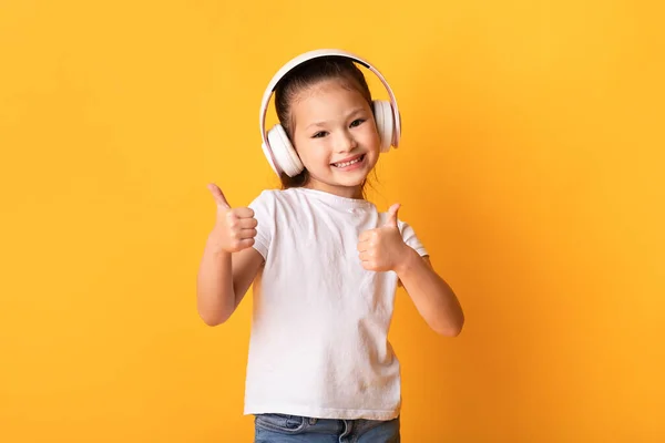 Smilende asiatisk jente som nyter musikk med hodetelefoner – stockfoto