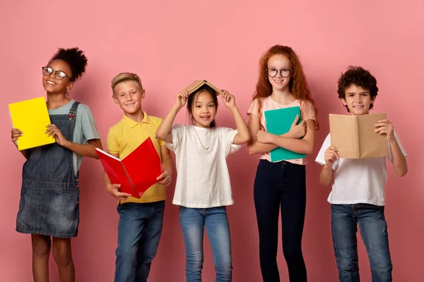 Educação escolar. Retrato de sorrir diversas crianças com livros e livros de cópia olhando para a câmera, fundo rosa — Fotografia de Stock