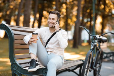 İş yerinde öğle yemeği molası. Kahve içmek ve cep telefonuyla konuşmak parktaki bankta bisikletle