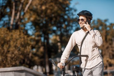 Güvenli bisiklet sürüşü. Kasklı gülen adam akıllı telefonla konuşuyor.