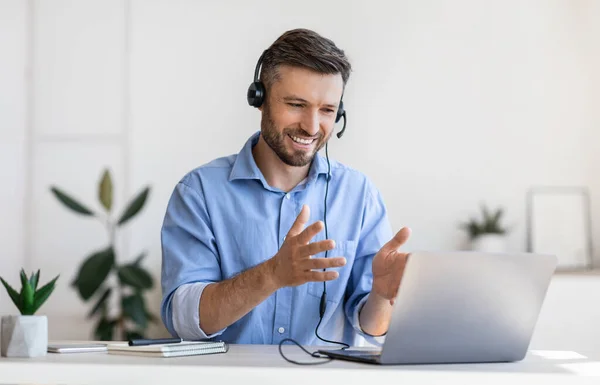 Videoconferentie. Vriendelijke man kantoormedewerker in headset met oproep op laptop — Stockfoto