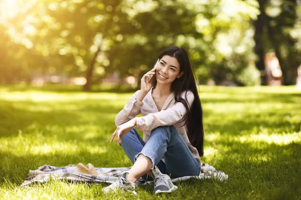 Llamada móvil. Sonriente chica coreana hablando en el teléfono celular mientras se relaja en el parque — Foto de Stock