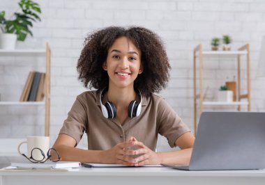 Çalışmak, çalışmak, evde tek başına eğitim görmek. Kulaklıklı ve dizüstü bilgisayarlı kız kameraya bakıyor.