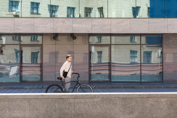 Jízda na kole ve městě. Mladý hipster s taškou procházky na kole — Stock fotografie