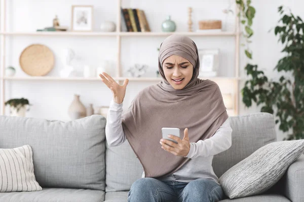 Verärgerte Araberin im Hijab, die zu Hause Smartphone in der Hand hielt, erhielt schlechte Nachricht — Stockfoto