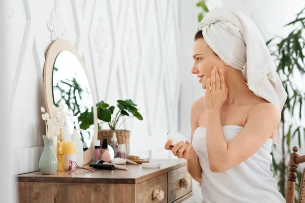 Chica bonita usando crema facial frente al espejo —  Fotos de Stock