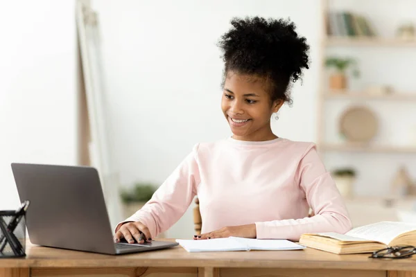 Afro-americana chica haciendo tarea en el ordenador portátil sentado en interiores —  Fotos de Stock