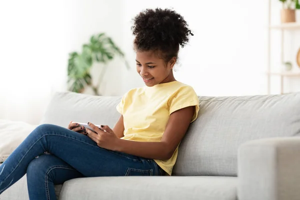 Afrikaans tiener meisje met behulp van telefoon zitten op de bank thuis — Stockfoto