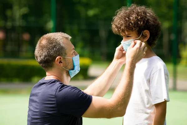 Babası çocuğuna yüz koruyucu bir maske takıyor.