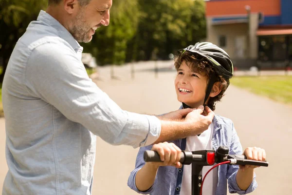 Adult man putting protective helmet on curly boy — Stock Photo, Image