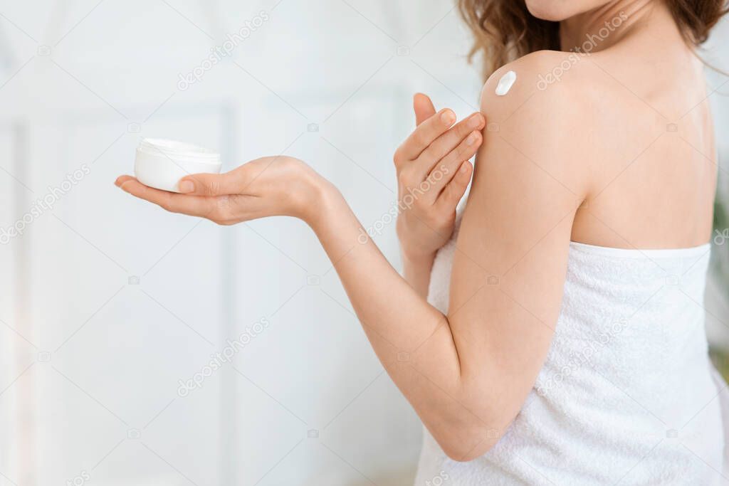 Unrecognizable woman holding jar, applying cream on her body