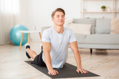 Yoga ve esneme egzersizleri. Paspasın üzerinde spor giyinen barışçıl bir adam egzersiz yapıyor.