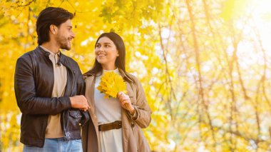 Gülen romantik çift sonbahar parkında yürüyor.