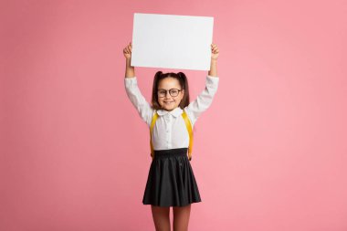 Okul için hazırlık. Sırt çantalı, gözlüklü, içi boş bir tabela tutan gülümseyen küçük kız.