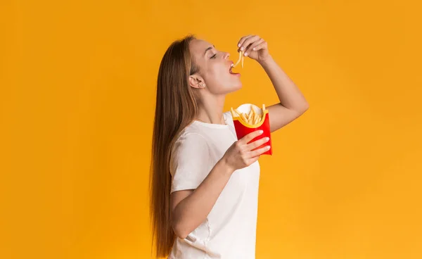 Głodny Millennial Girl Jedzenie frytki serwowanie, Stojąc nad żółtym tle — Zdjęcie stockowe