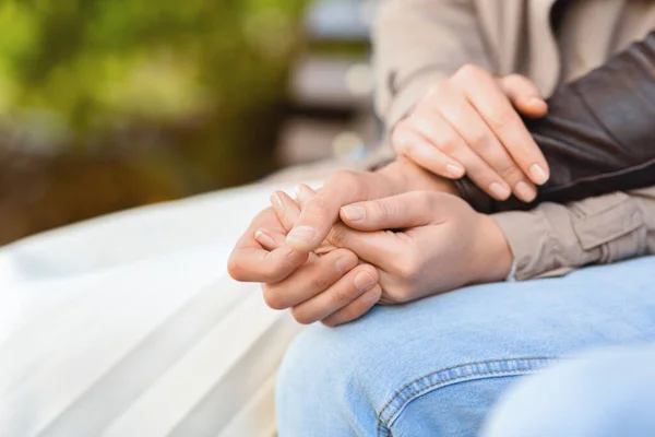 Kvinna håller man hand med båda händerna, sitter på bänken — Stockfoto