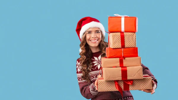 Compras de Navidad. Chica encantadora en suéter cálido y Santa sombrero celebración pila de cajas de regalo sobre fondo azul, espacio de copia — Foto de Stock