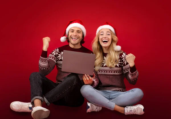 フル長さの肖像画の千年のカップルでクリスマス服ジェスチャーはいラップトップコンピュータの近くに赤の背景 — ストック写真