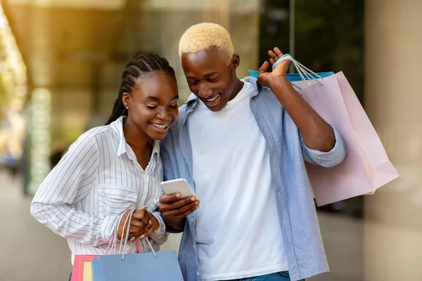 Advertentie over verkoop op smartphone. glimlachende Afrikaan amerikaanse man en meisje kijken naar telefoon — Stockfoto