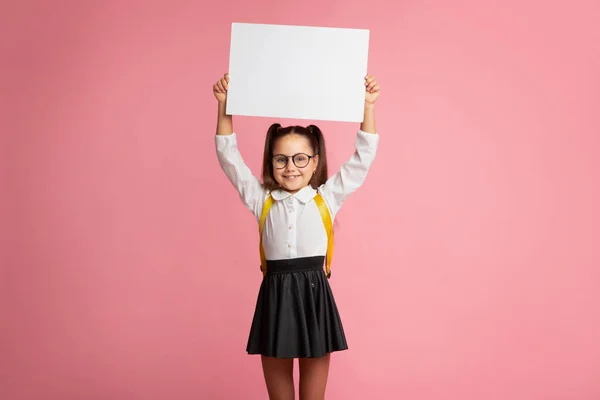 Felkészülés az iskolára. Mosolygó kislány hátizsákkal a szemüvegben, kezében jel üres hely — Stock Fotó