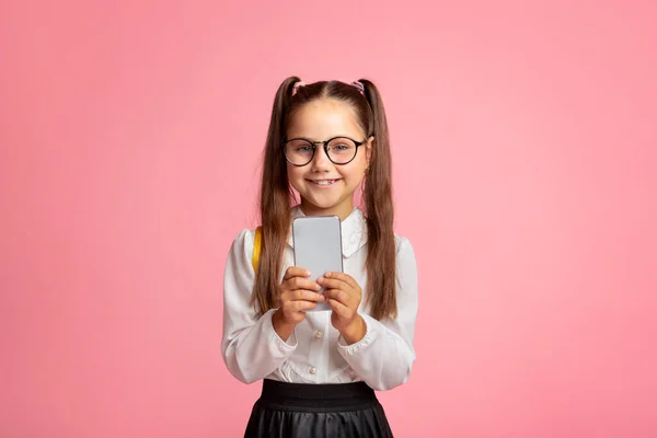 Moderní technologie a škola. Usmívající se holčička s brýlemi drží smartphone — Stock fotografie