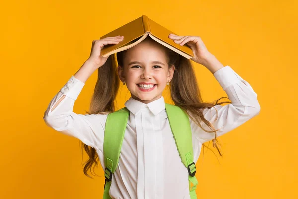 Studentessa tenendo libro sulla testa sorridente alla macchina fotografica, Studio girato — Foto Stock