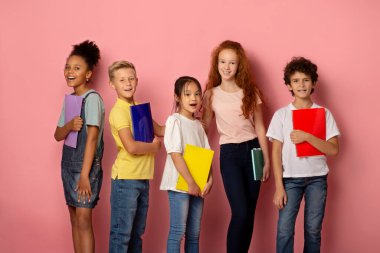 Okul eğlenceli bir şey. Heyecanlı çeşitli öğrenciler pembe arka planda not defterleri tutuyorlar.