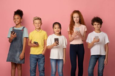 Pembe arka planda çalışmak için cep telefonu kullanan çok ırklı çocukların portresi