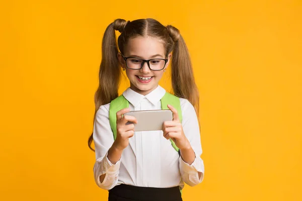 Školní dívka hraje mobilní hru na telefonu přes žluté pozadí — Stock fotografie