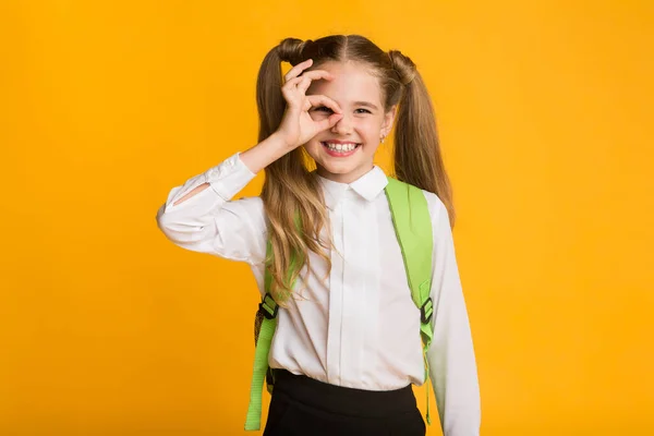 Grappig schoolmeisje Gesturing OK Sign Staande over gele achtergrond, Studio — Stockfoto