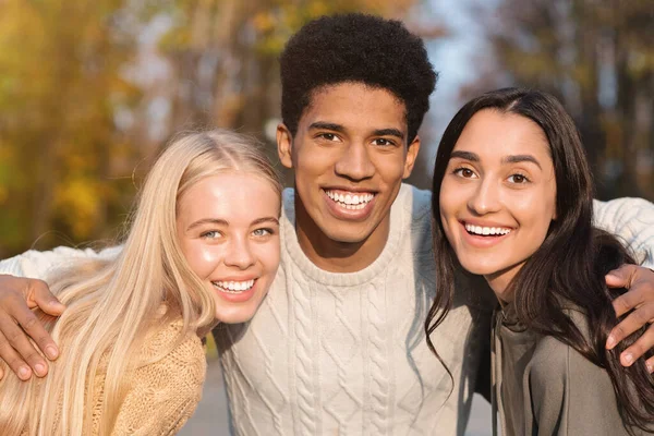 Портрет трех многонациональных друзей, улыбающихся на фоне парка — стоковое фото
