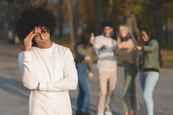 Multiracial teenagers pointing at frustrated black guy — Stock Photo, Image
