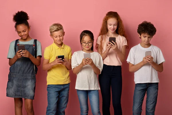 Csoport változatos iskolások ragadt mobiltelefonok tanul online rózsaszín háttér — Stock Fotó