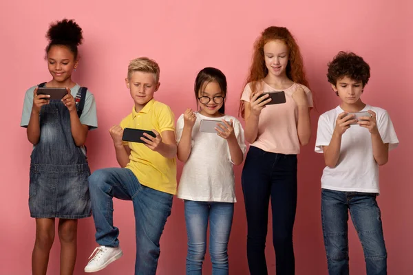 Alunos alegres jogando jogos móveis em seus telefones sobre fundo rosa — Fotografia de Stock