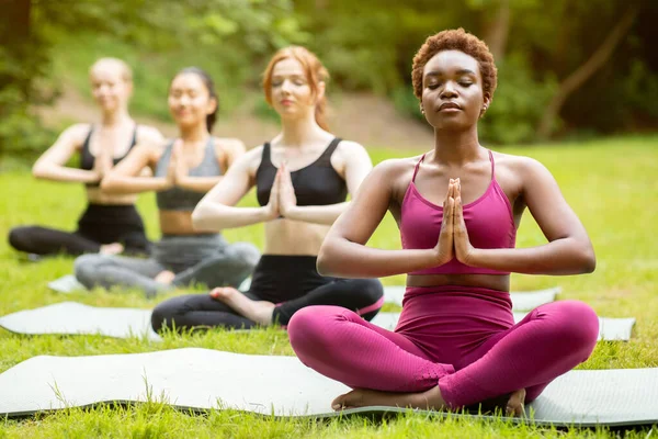 Йога для внутреннего покоя. Различные молодые девушки медитируют в позе лотоса и делают жест намасте в парке — стоковое фото