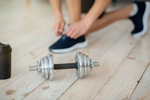 Start training at home during quarantine. Guy ties laces on sneakers, on floor in interior — Stock Photo, Image