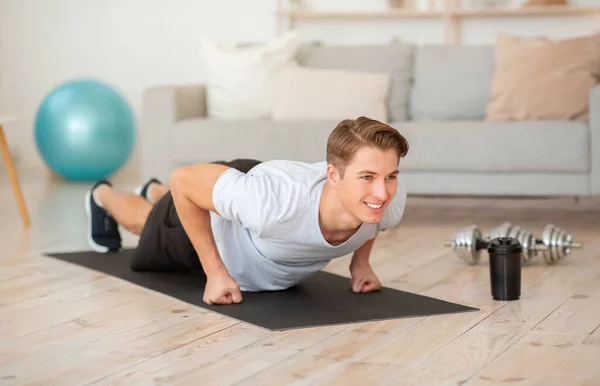 Sport während Quarantäne und Selbstisolierung. Glücklicher Kerl macht Liegestützübungen im Wohnzimmer — Stockfoto