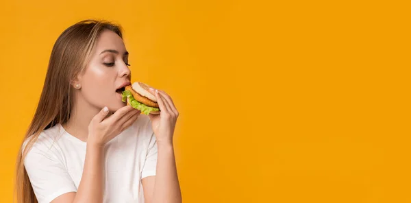 Нездорове харчування. Молода жінка їсть фастфуд, насолоджуючись смачним бургером — стокове фото