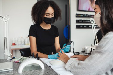 Profesyonel Afro-Amerikan koruyucu maske ve eldiven ustası elektrikli tırnak cilası yöntemi kullanıyor.